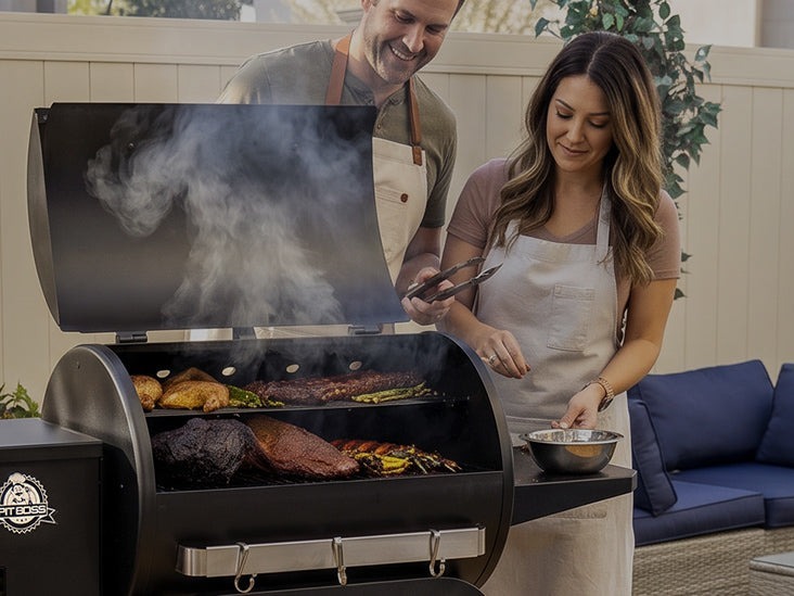 A wood pellet grill with the lid open on an outdoor wood deck