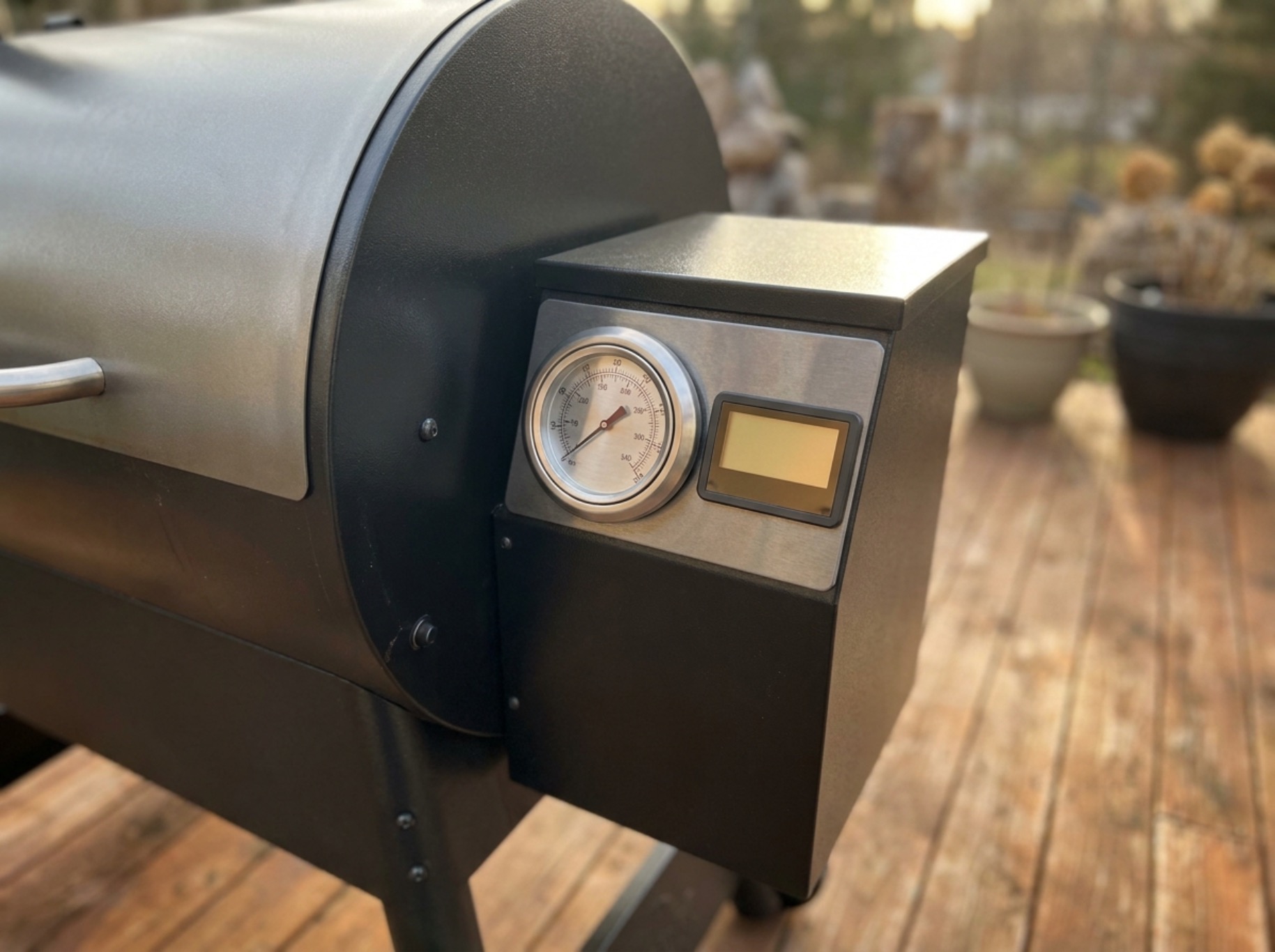 Stainless steel pellet grill control panel with digital display and dial, on an outdoor patio
