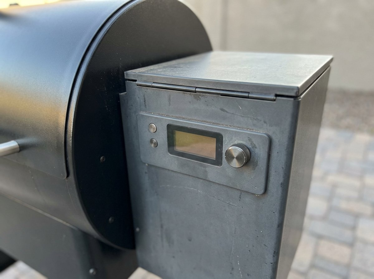 Close-up of a pellet grill controller with a small display, two buttons and a dial