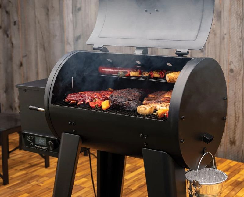 A wood pellet grill with the lid open on an outdoor wood deck
